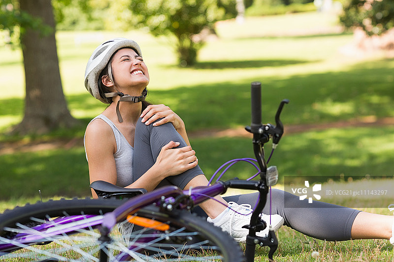年轻女骑行者腿部受伤坐在公园草地上图片素材