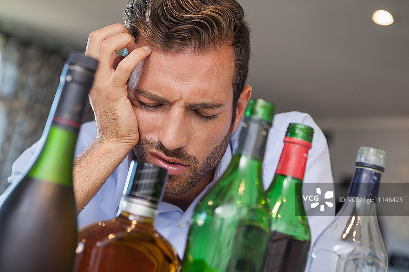 醉酒的商人倒在当地酒吧的许多烈酒瓶旁图片素材