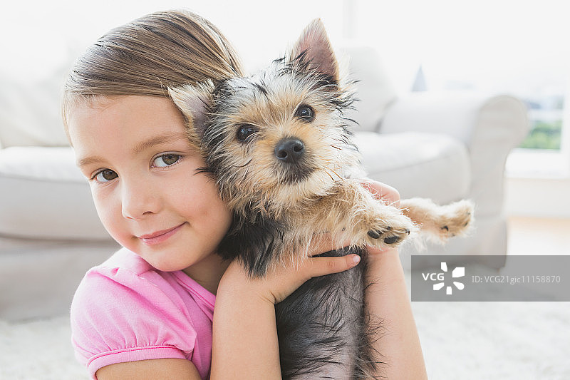 微笑的小女孩抱着她的约克夏犬幼犬，在客厅里图片素材