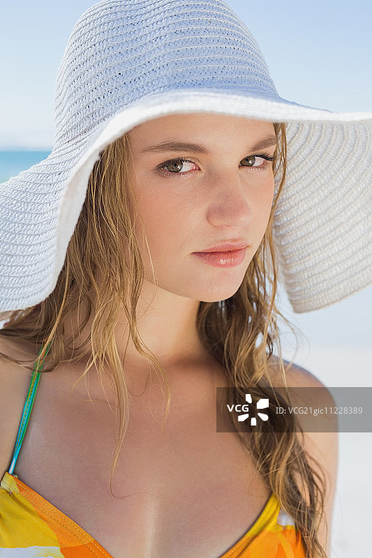 阳光明媚的日子里，戴着白色草帽和比基尼在海滩上微笑的美丽女人图片素材