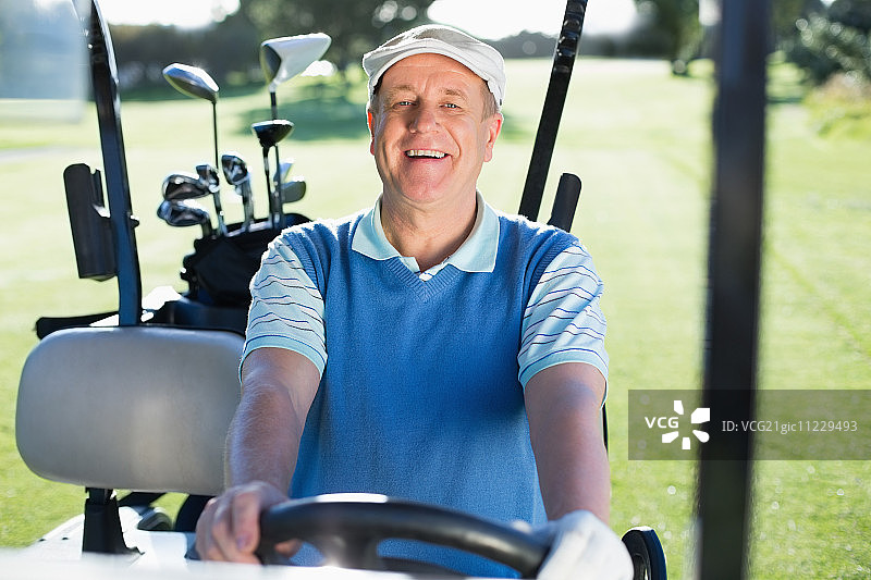 阳光明媚的高尔夫球场上，快乐的高尔夫球手驾驶着高尔夫球车对着镜头微笑图片素材
