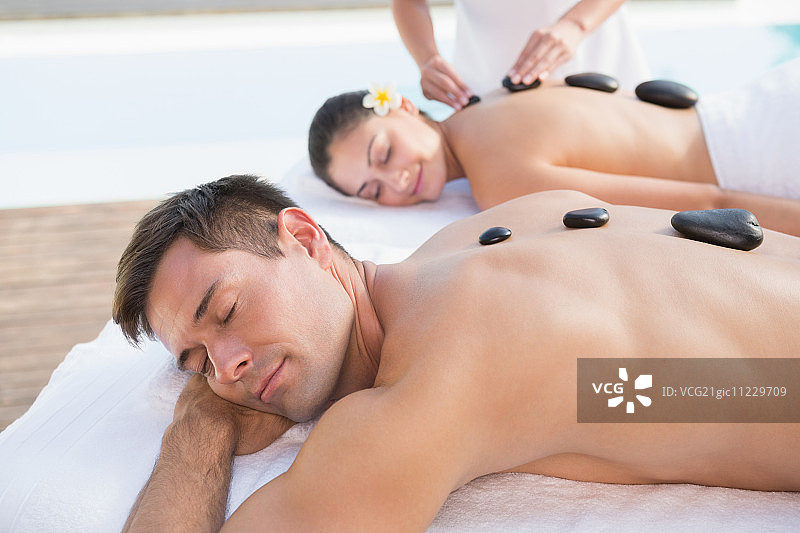 在水疗中心泳池外享受热石按摩的迷人情侣图片素材