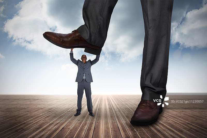 多云天空背景下踩在小商人身上的商人合成图像图片素材