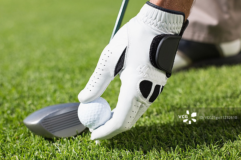 高尔夫球手在阳光明媚的高尔夫球场上将高尔夫球放在球座上图片素材