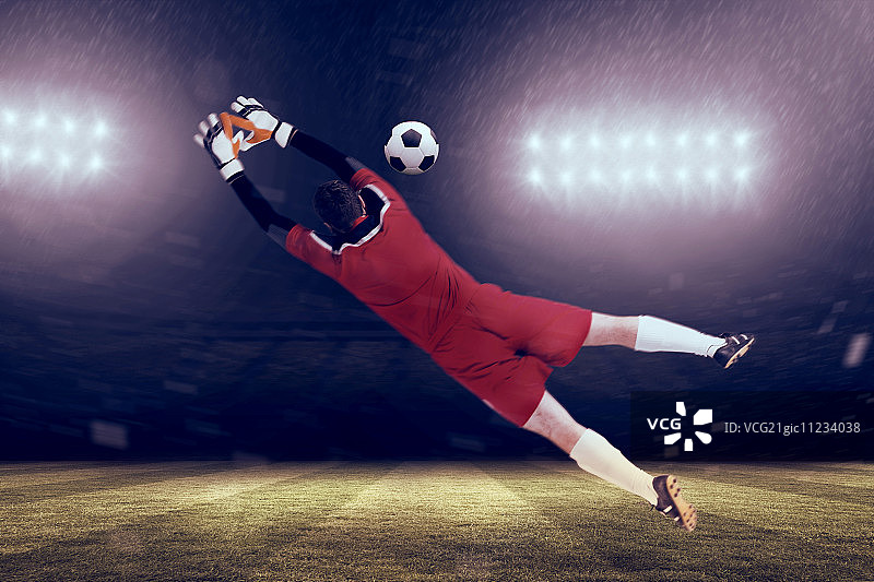 聚光灯下，身穿红色球衣的守门员跃向足球场图片素材