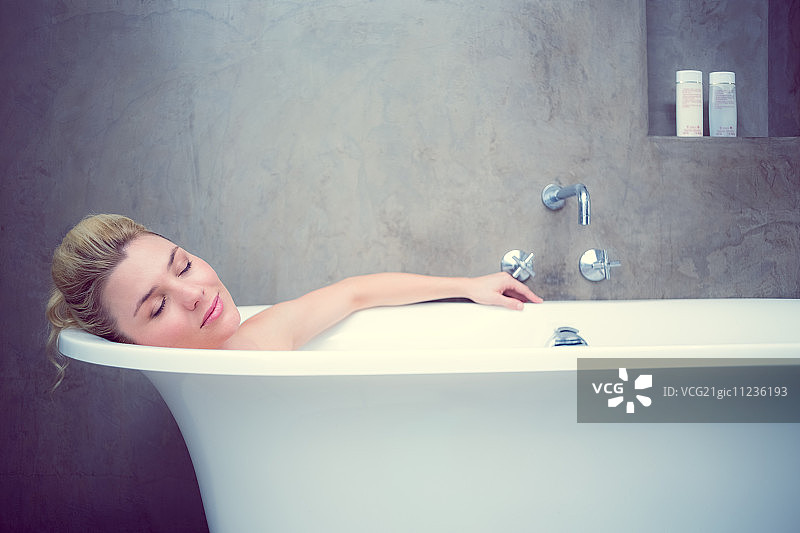 宁静的金发女人在家中浴室的浴缸里图片素材