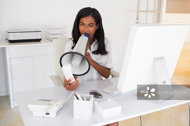 愤怒的女商人对着办公室里的电话用扩音器喊叫图片素材