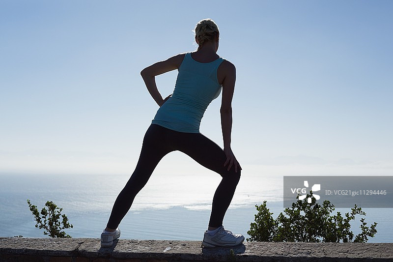 健身女人：阳光明媚的日子里，伸展双腿眺望大海图片素材