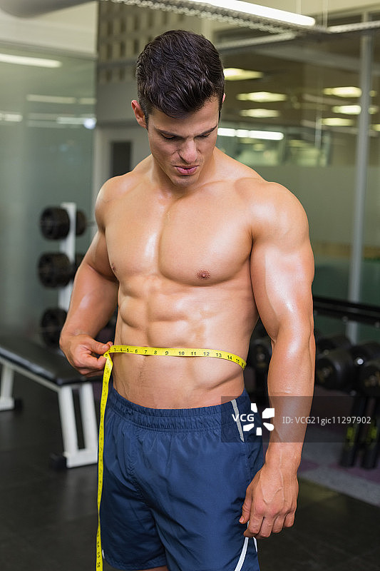 赤膊健壮的男人在健身房测量腰围图片素材