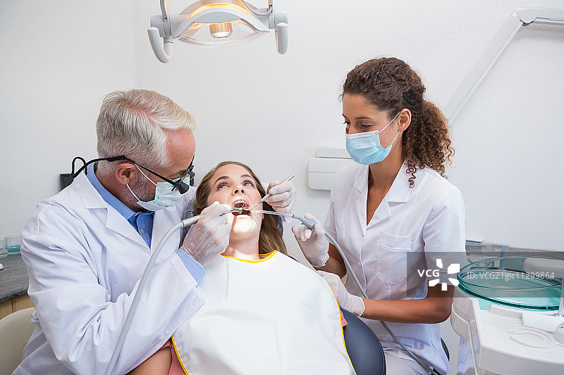 牙医在牙科诊所的牙椅上与助手一起检查病人的牙齿图片素材