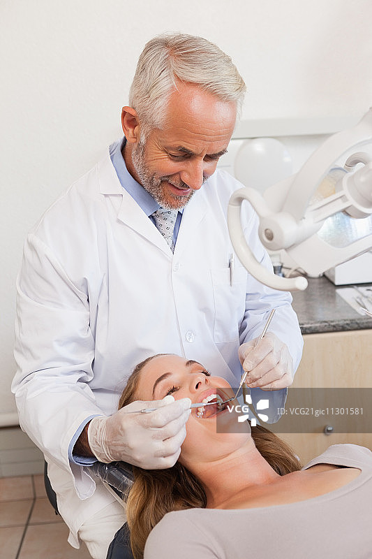 牙医在牙科诊所的牙椅上检查患者的牙齿图片素材