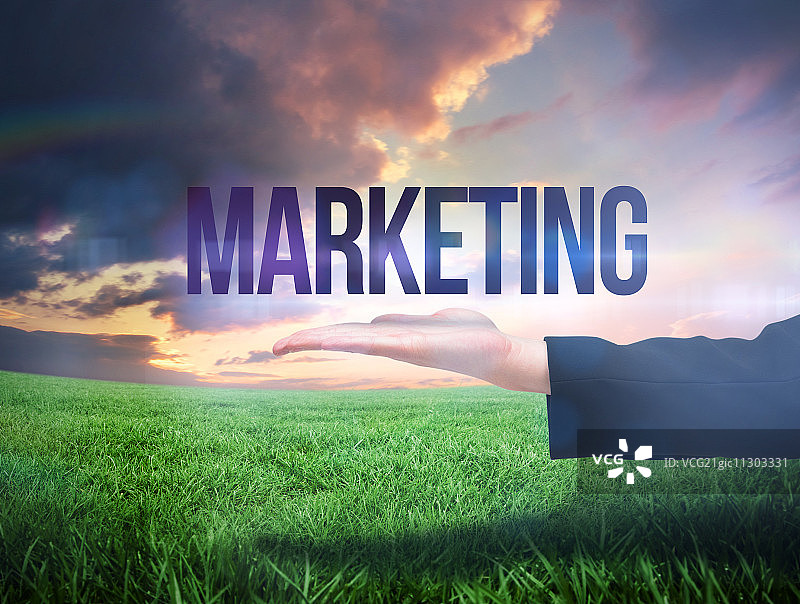 女商人手指指向绿色田野橙色天空下的“营销”字样图片素材