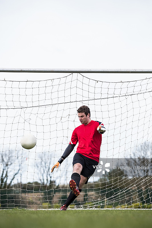 晴朗的一天，红色守门员将球踢离球门图片素材