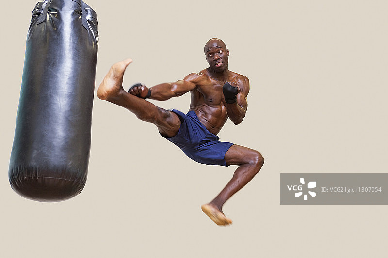 赤膊健壮的拳击手踢打白色背景上的沙袋全身照图片素材