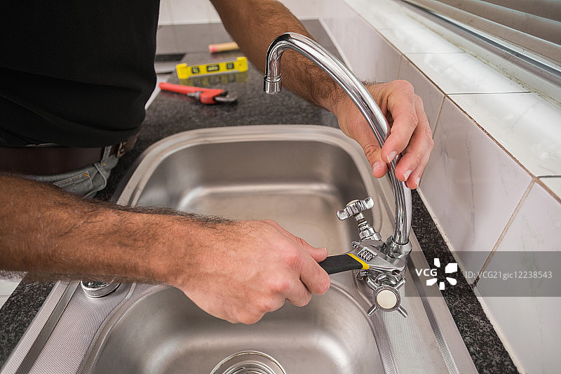 水管工在厨房用扳手修理水槽图片素材