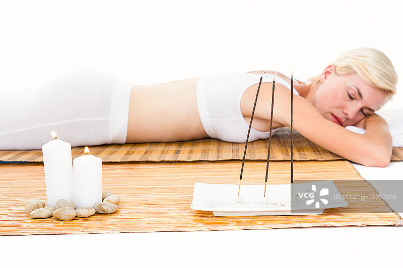 躺在白色背景竹席上的迷人金发女人图片素材