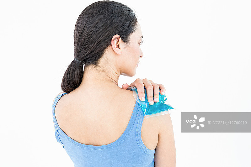 在白色背景下，将冰袋敷在肩膀上的美丽深发色女子图片素材