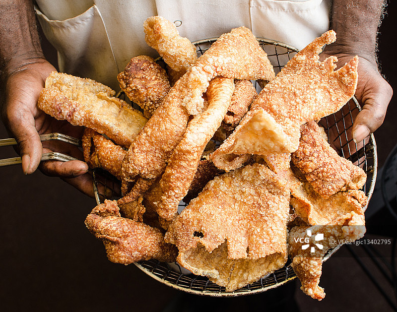 男人拿着漏勺装着炸猪皮图片素材