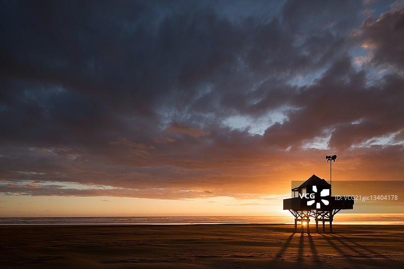 新西兰北岛贝壳海滩日落时救生员小屋的剪影图片素材