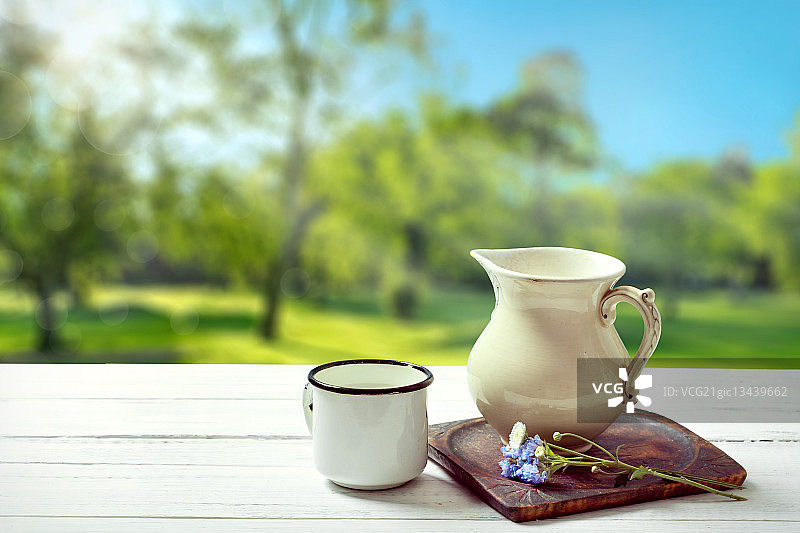 阳光明媚的夏日乡村背景下的牛奶罐和马克杯图片素材