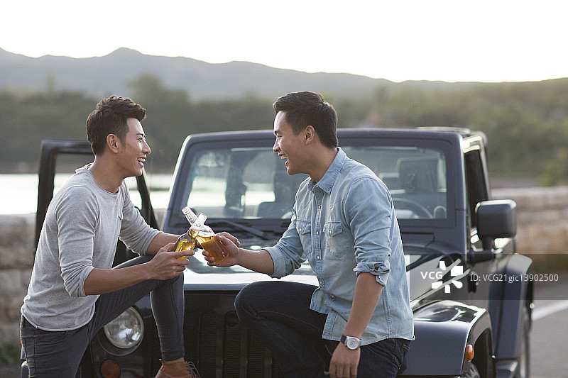 年轻人在吉普车旁喝啤酒图片素材