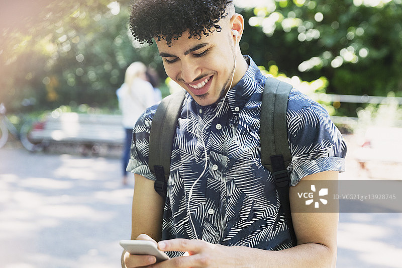 戴着耳机用MP3播放器听音乐的卷发微笑男人图片素材