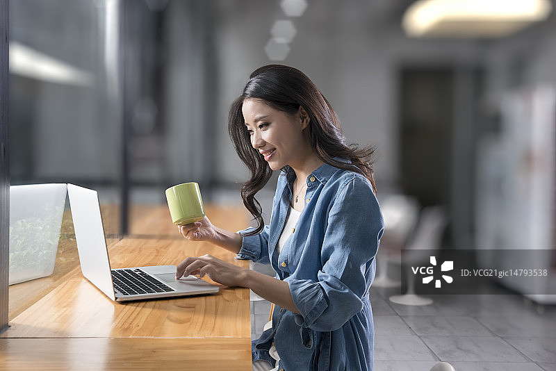 Creative businesswoman using laptop in break room图片素材