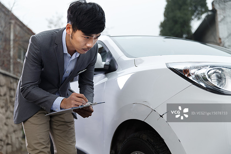 青年男人在记录被划了的汽车的情况图片素材
