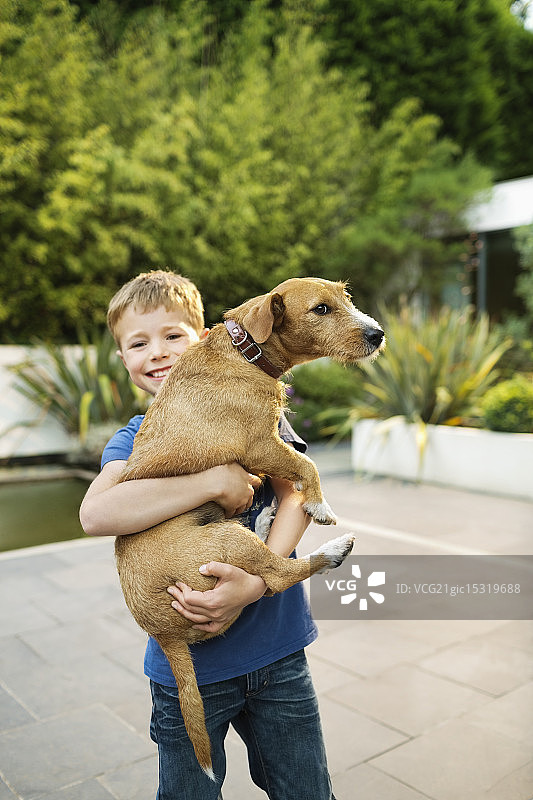 户外抱着小狗的微笑男孩图片素材