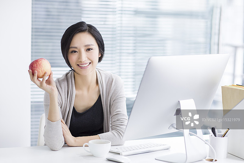 年轻女子在办公室拿着一个苹果图片素材