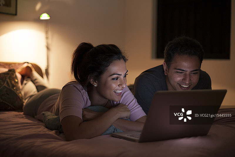 新加坡情侣夜晚在床上用笔记本电脑放松图片素材