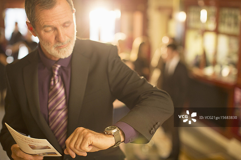 穿着考究的男人在剧院大厅查看时间，手中拿着节目单特写图片素材