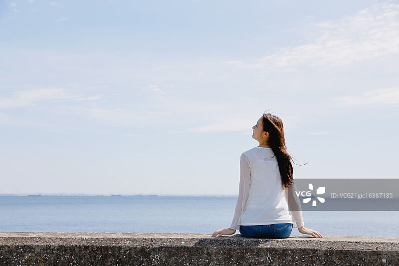 年轻的日本女人坐在海边的水泥墙上图片素材