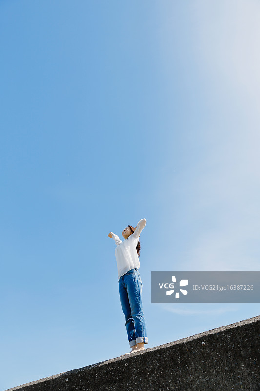 站在海边水泥墙上的年轻日本女子图片素材
