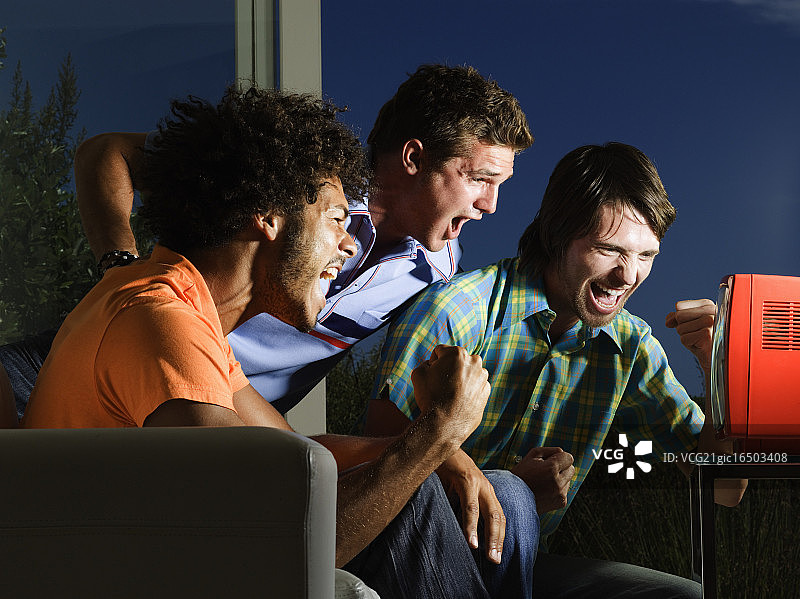 三位激动的体育迷正在看电视图片素材