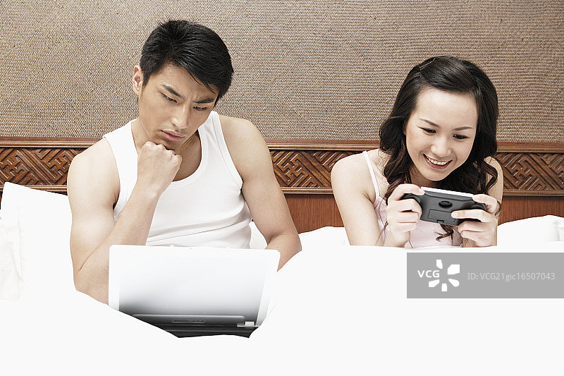 情侣在床上看移动设备图片素材