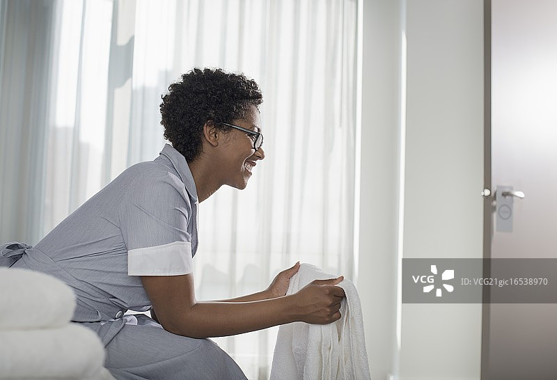 在酒店房间里拿着毛巾的微笑女佣图片素材