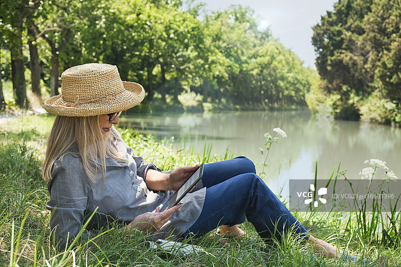 法国，躺在河岸边阅读电子书的女人图片素材