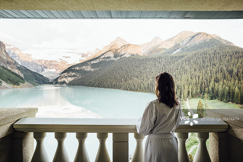 年轻女子身穿浴袍在路易斯湖的阳台上眺望，加拿大艾伯塔省班夫国家公园图片素材
