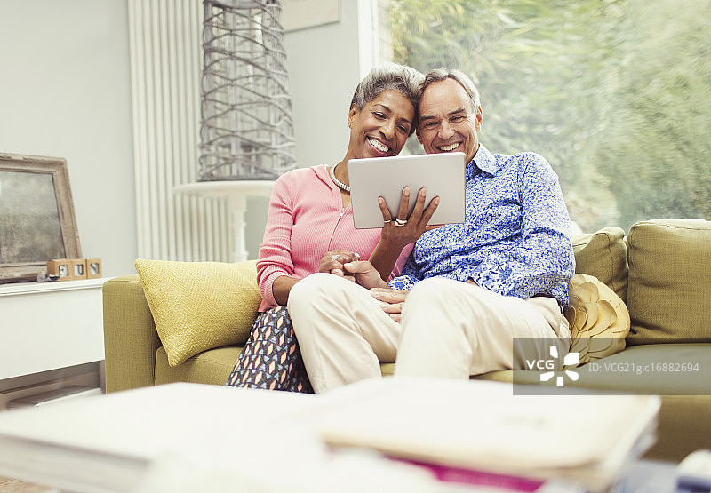 微笑的中年夫妇在客厅沙发上使用平板电脑图片素材