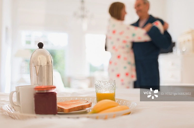 年长的夫妇穿着浴袍在床上享用早餐时跳舞图片素材