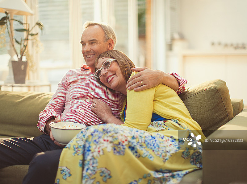 充满爱意的中年夫妇在客厅沙发上看电视吃爆米花图片素材