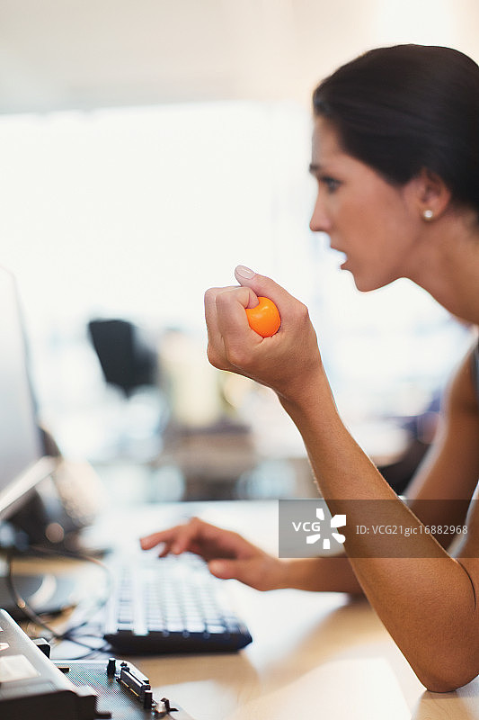 在办公室电脑前挤压压力球的女商人图片素材