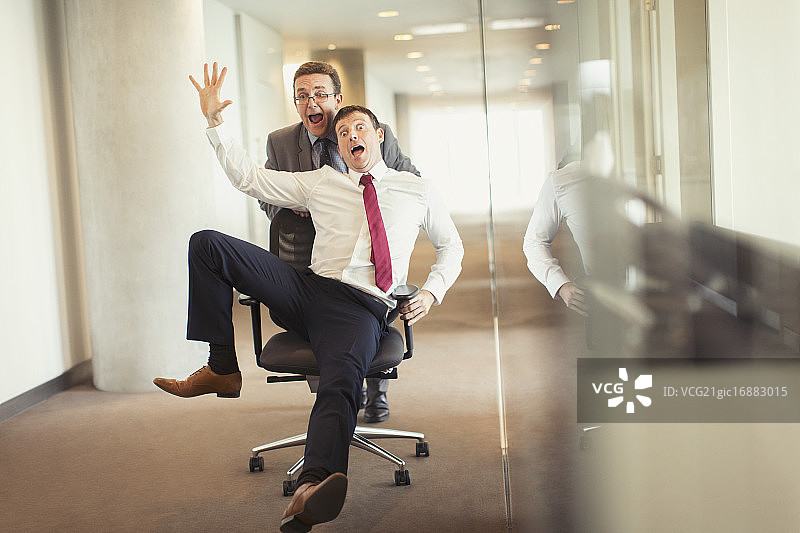 在办公室里，有趣的商人把同事从走廊的椅子上推下去图片素材