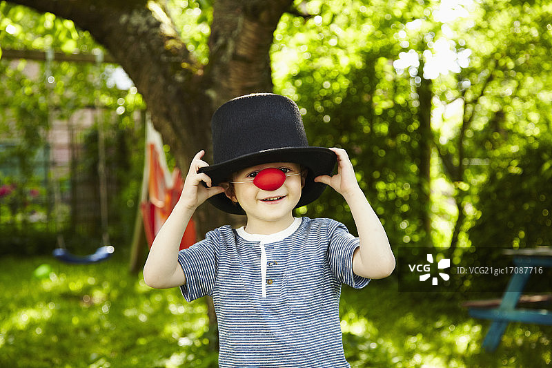 装扮成小丑的红发男孩（4-5岁）的特写，戴着红鼻子和高顶帽子图片素材