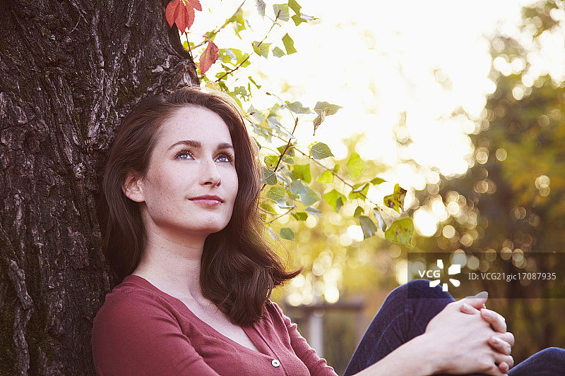 坐在公园树旁的年轻女子肖像，逆光图片素材