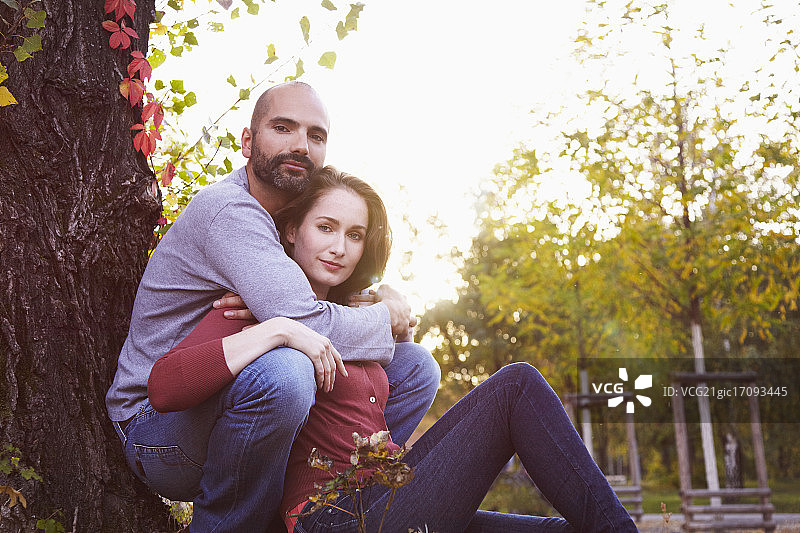 幸福情侣倚靠树干拥抱的逆光肖像图片素材