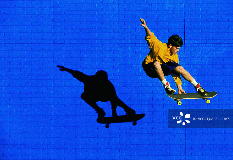 滑板运动员飞过蓝色砖墙图片素材