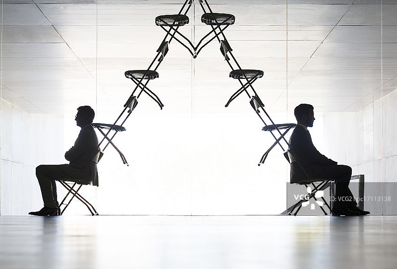 商人坐在办公椅装置艺术的两端图片素材