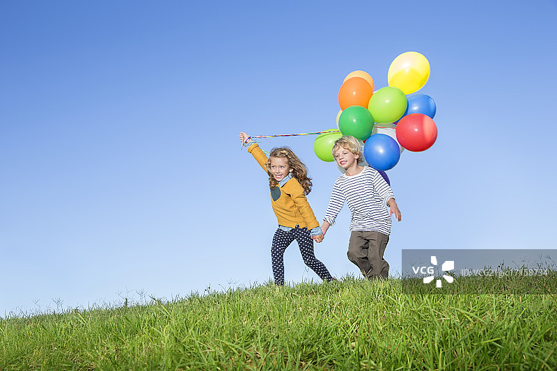 在草山上拿着一束气球的儿童图片素材
